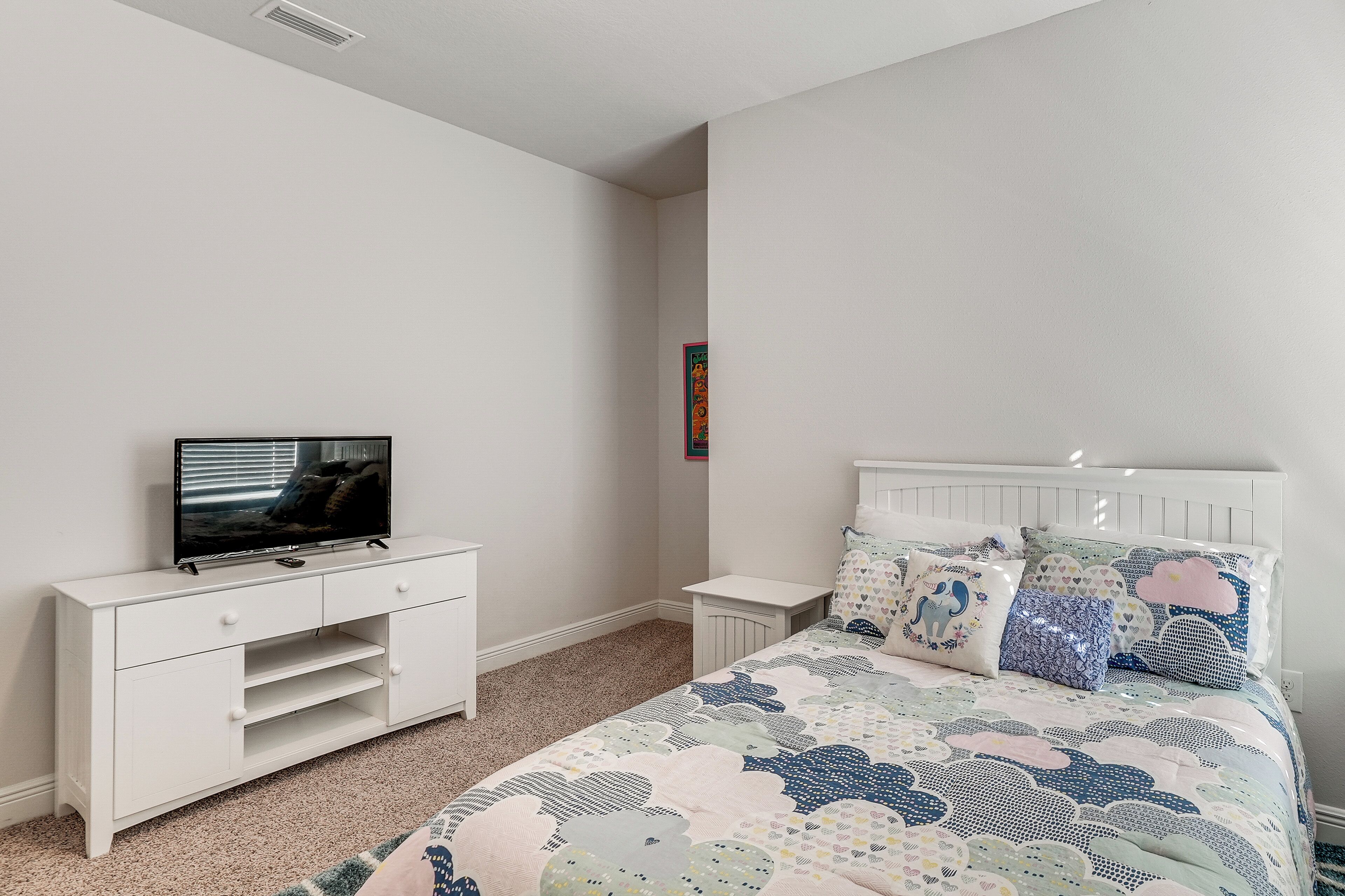 A bedroom with a bed, a TV on a white dresser, and a small bedside table.