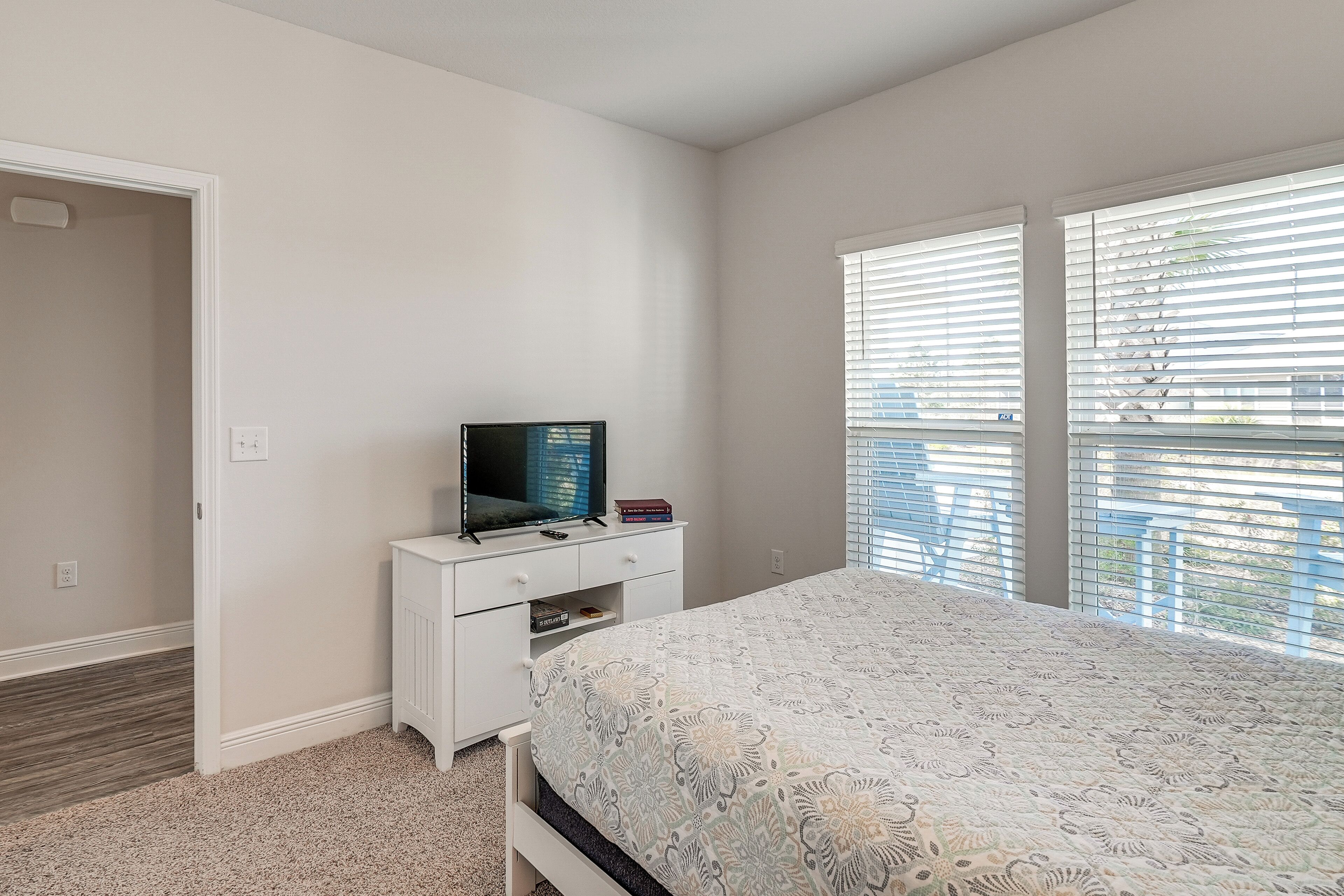 A bedroom with a bed, a TV on a dresser, and a window with blinds.