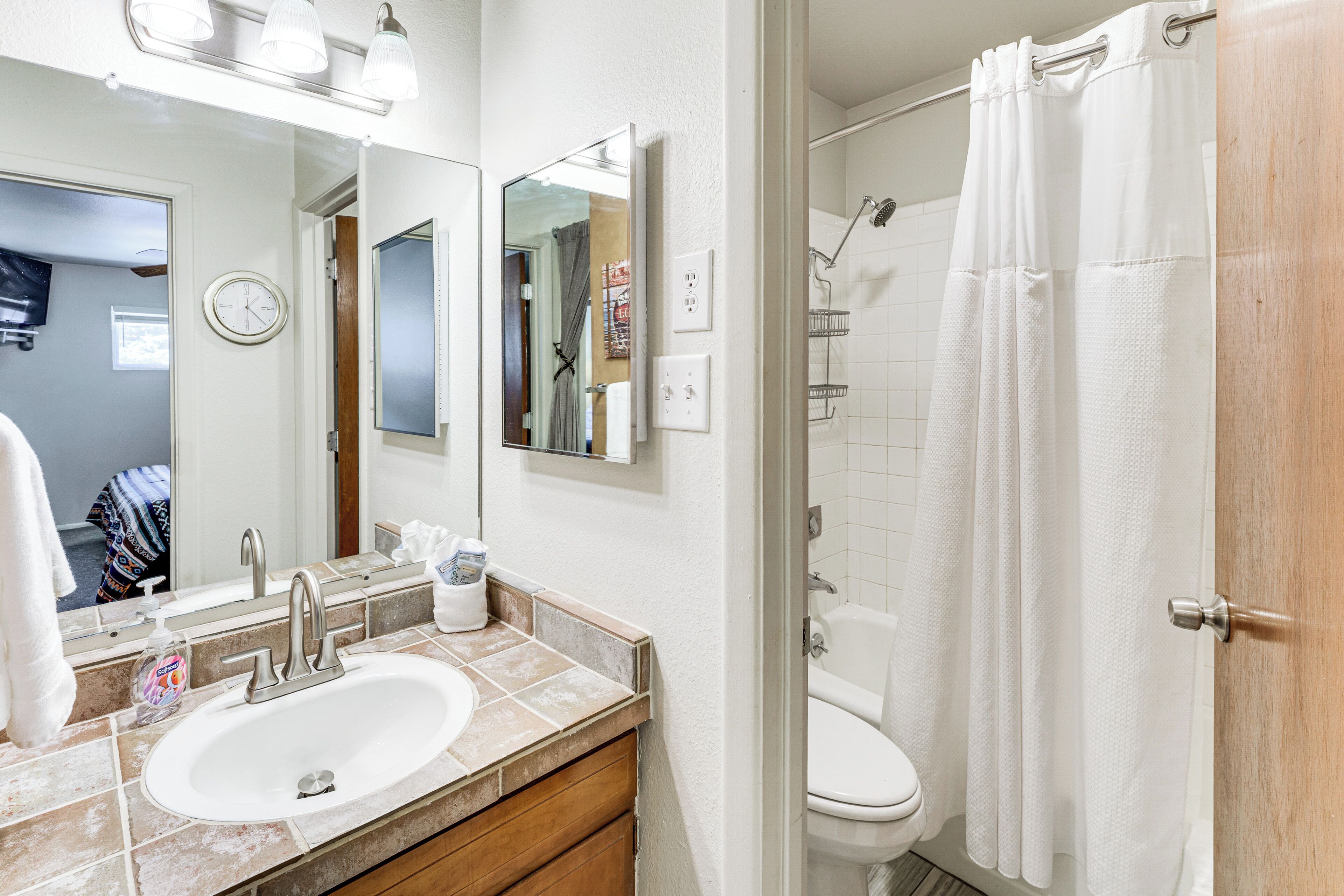 A bathroom with a sink, mirror, shower, and toilet.