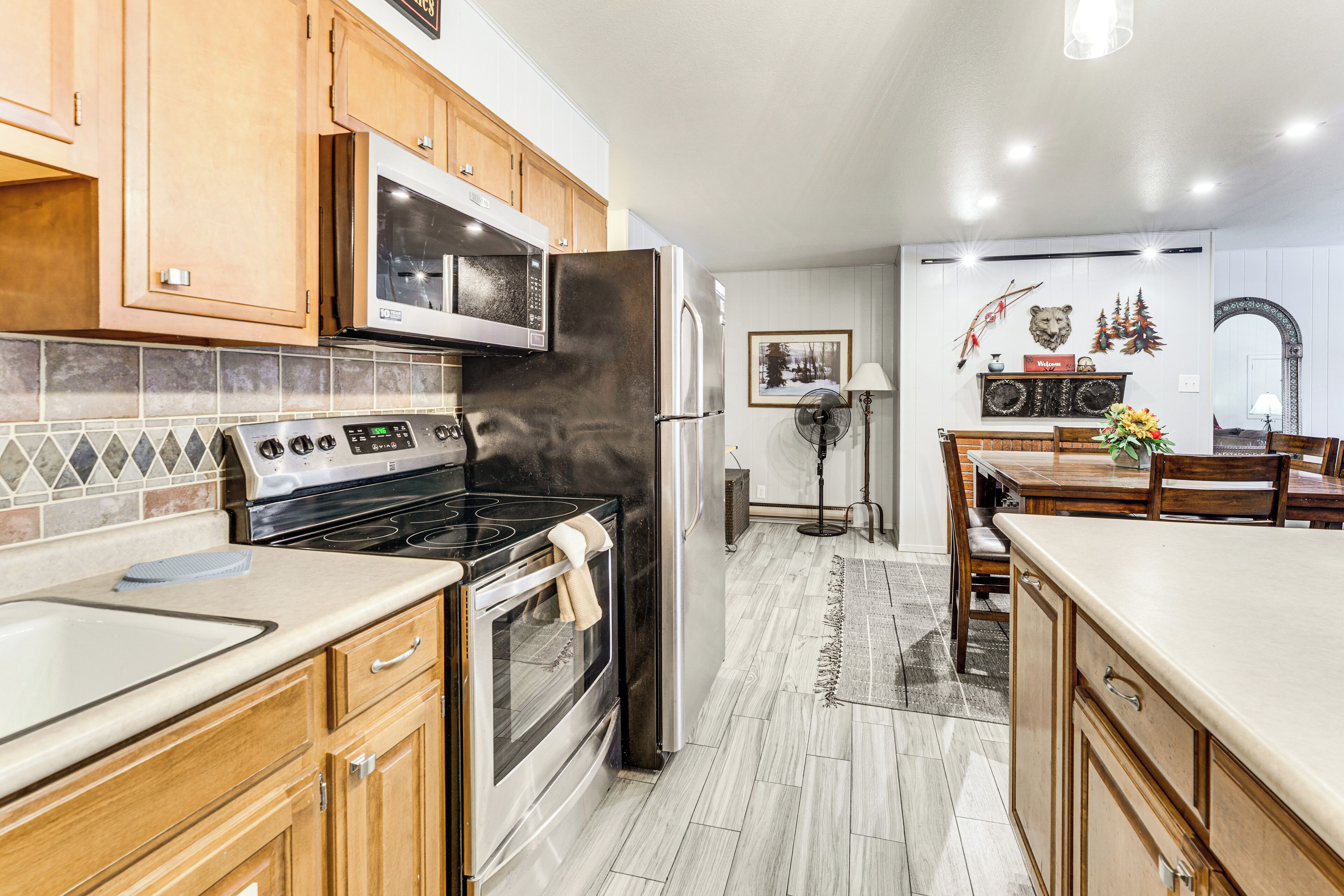 A modern kitchen with wooden cabinets, a stainless steel refrigerator, a microwave, and an oven.