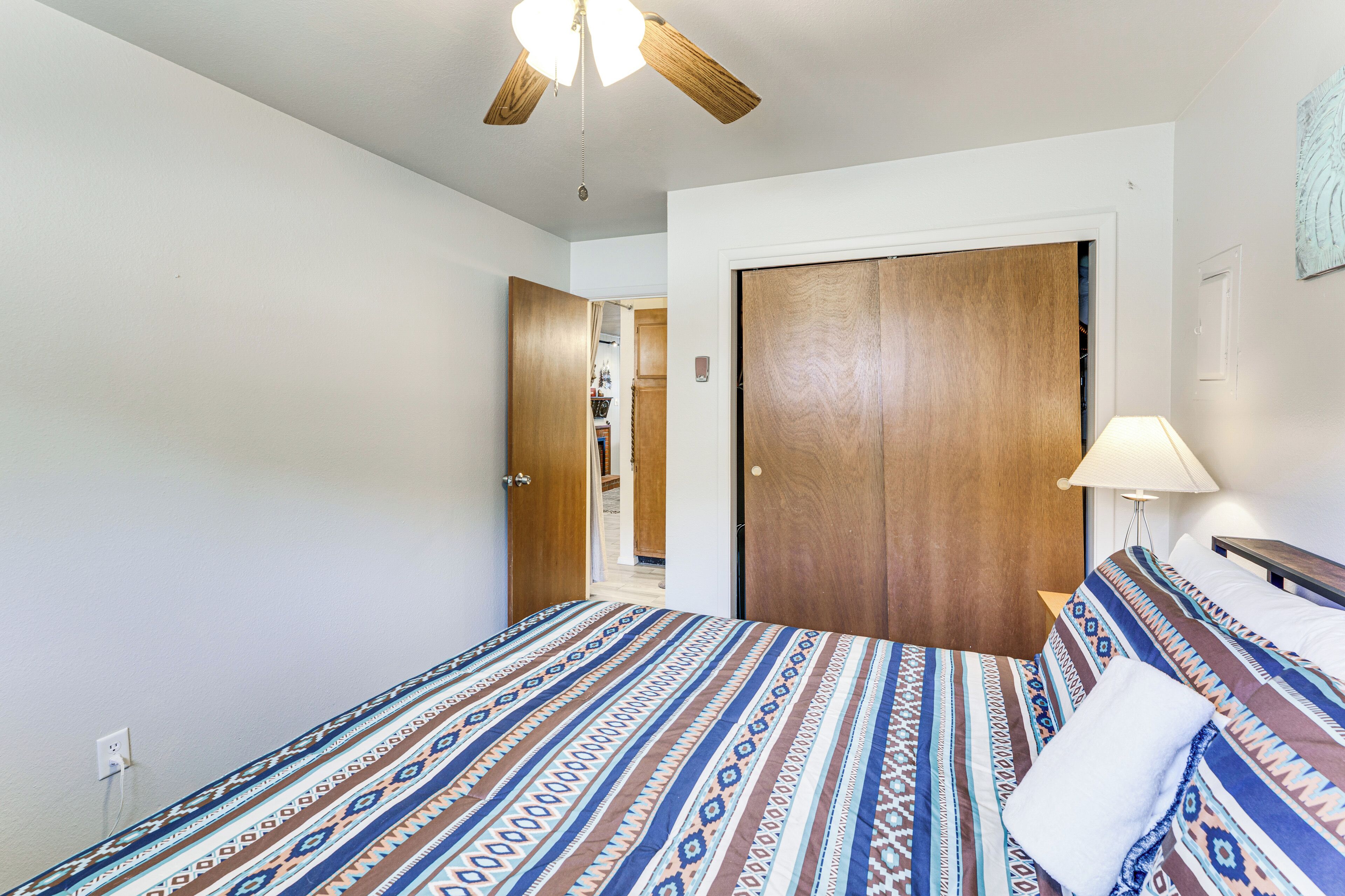 A bedroom with a bed, a ceiling fan, a wooden door, and a nightstand with a lamp.
