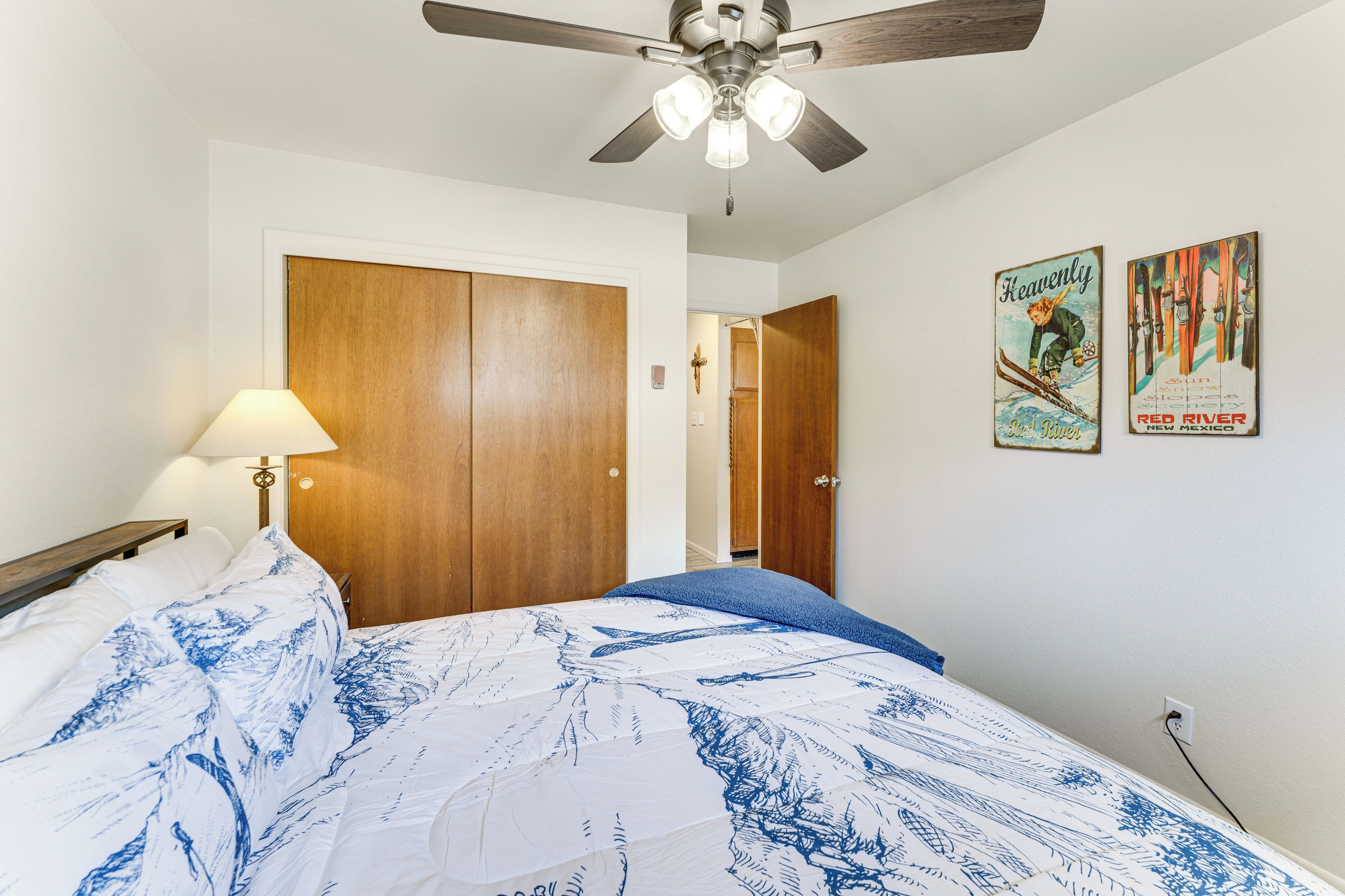 A bedroom with a bed, a ceiling fan, wooden wardrobe, and two wall posters.