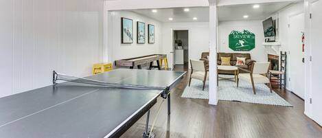 Habitació amb taula de ping-pong, sofà i taula de menjador amb cadires. Se veu una zona de cuina al fons.