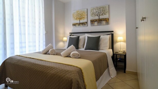 A hotel room with a bed, two bedside lamps, a window with curtains, and two wall art pieces. - Thyme Out - Modern Apartment in Egaleo/Athens (Egaleo)