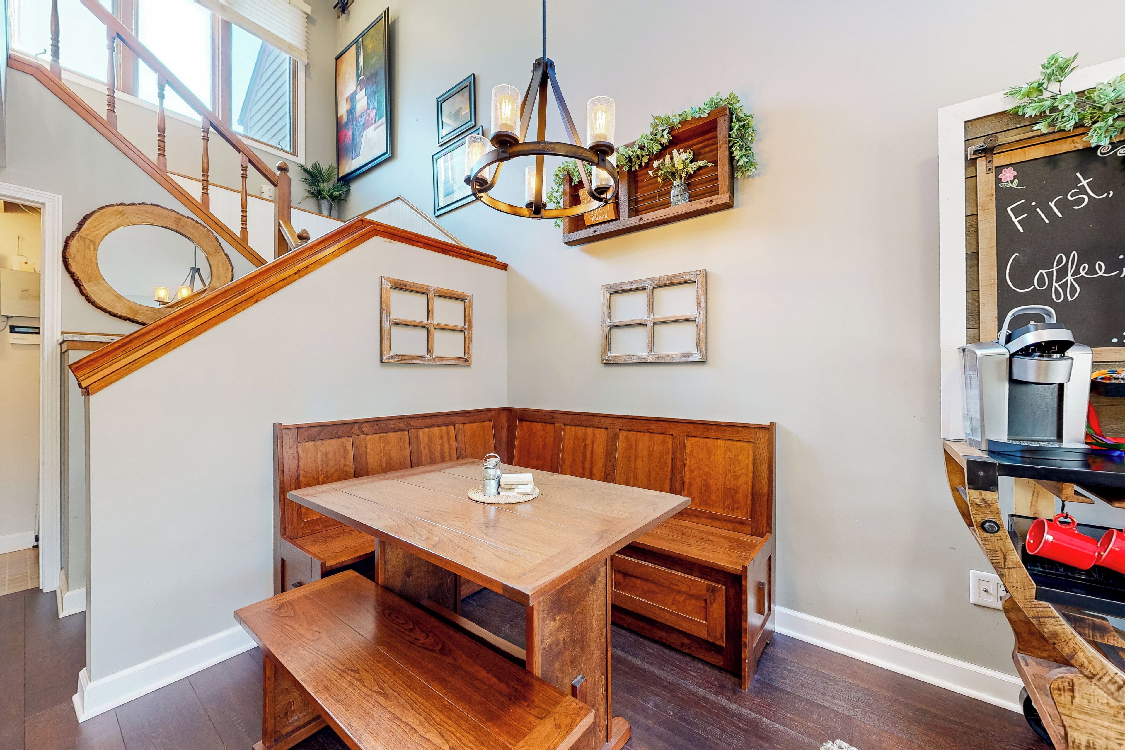 A cozy corner with a wooden bench and table, a chalkboard with 'First Coffee' written on it, and a staircase with wooden railings.