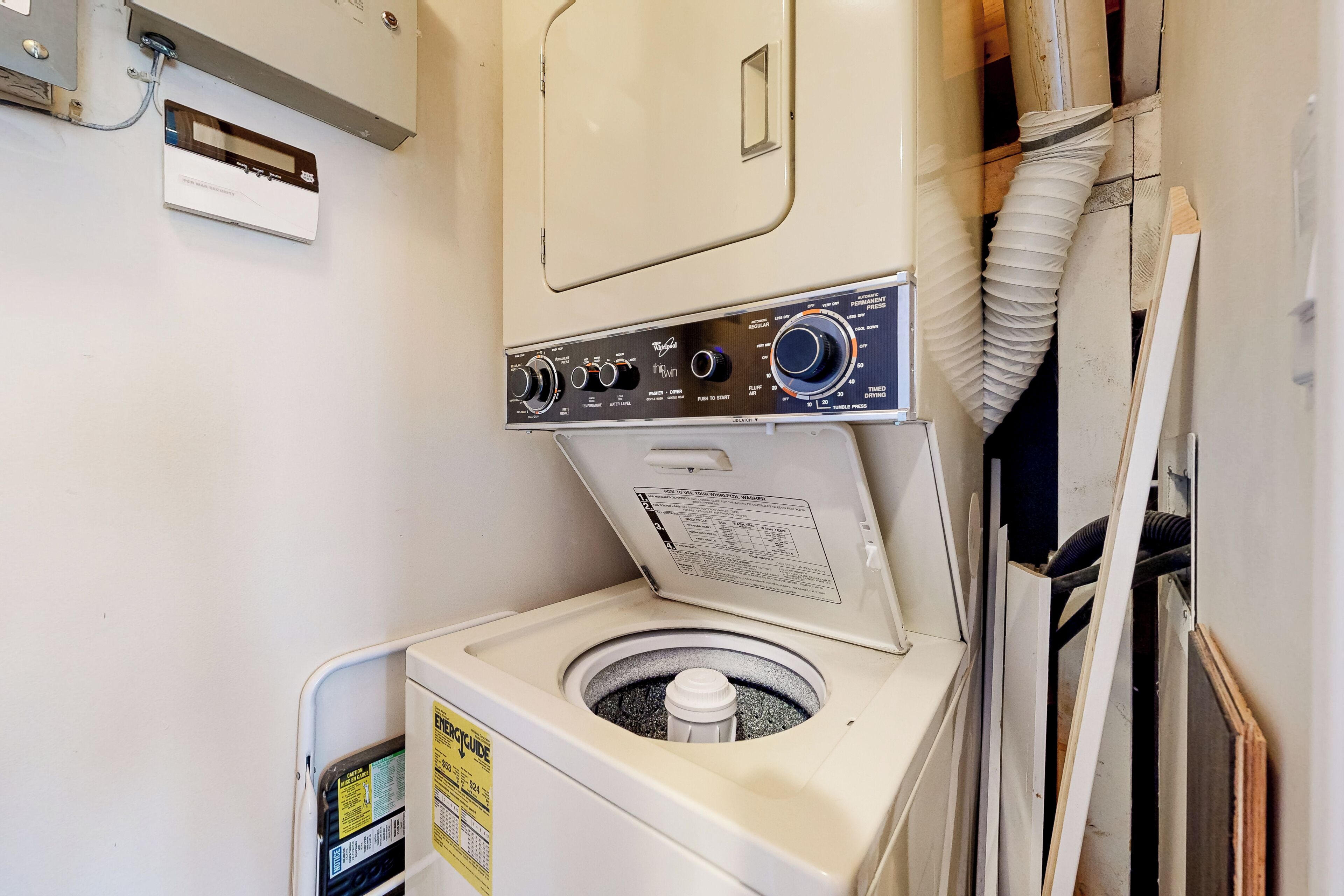 En kompakt, vit tvättmaskin med en kontrollpanel, ett litet förvaringsutrymme och en ventilationsslang.