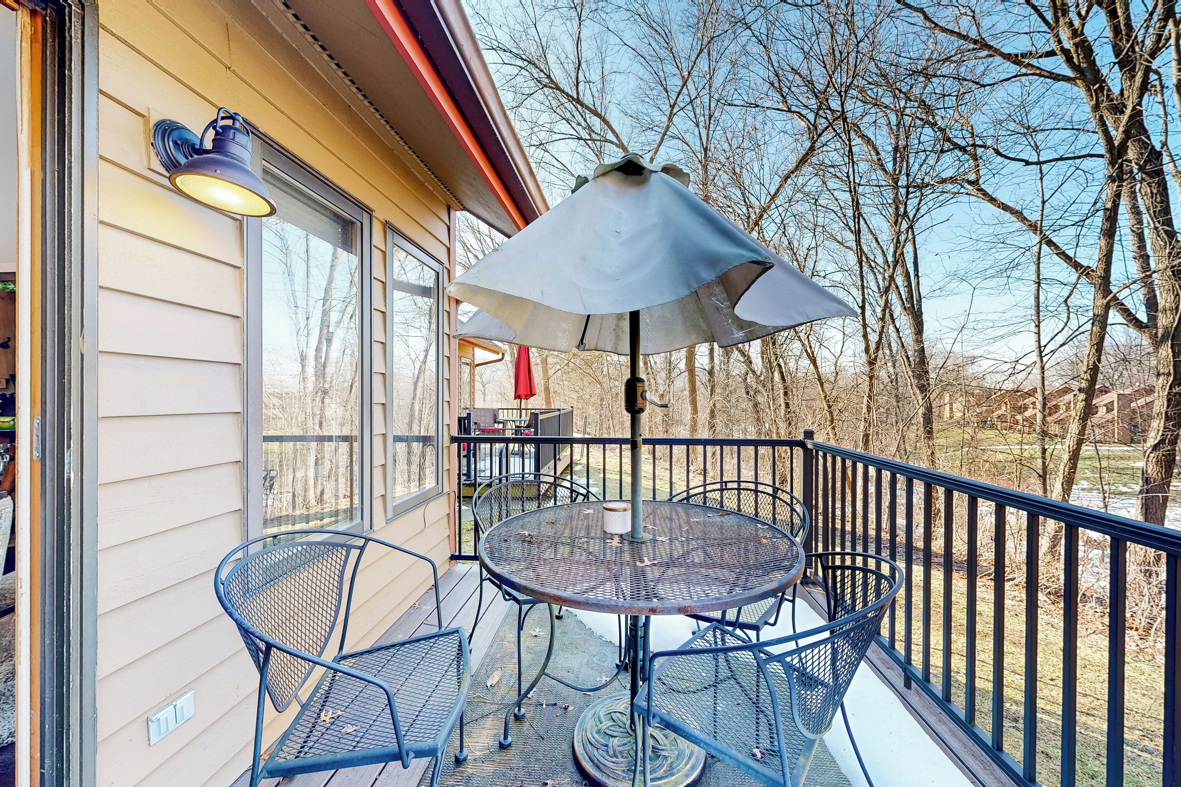 Een metalen tafel en stoelen op een balkon, met een metalen parasol.