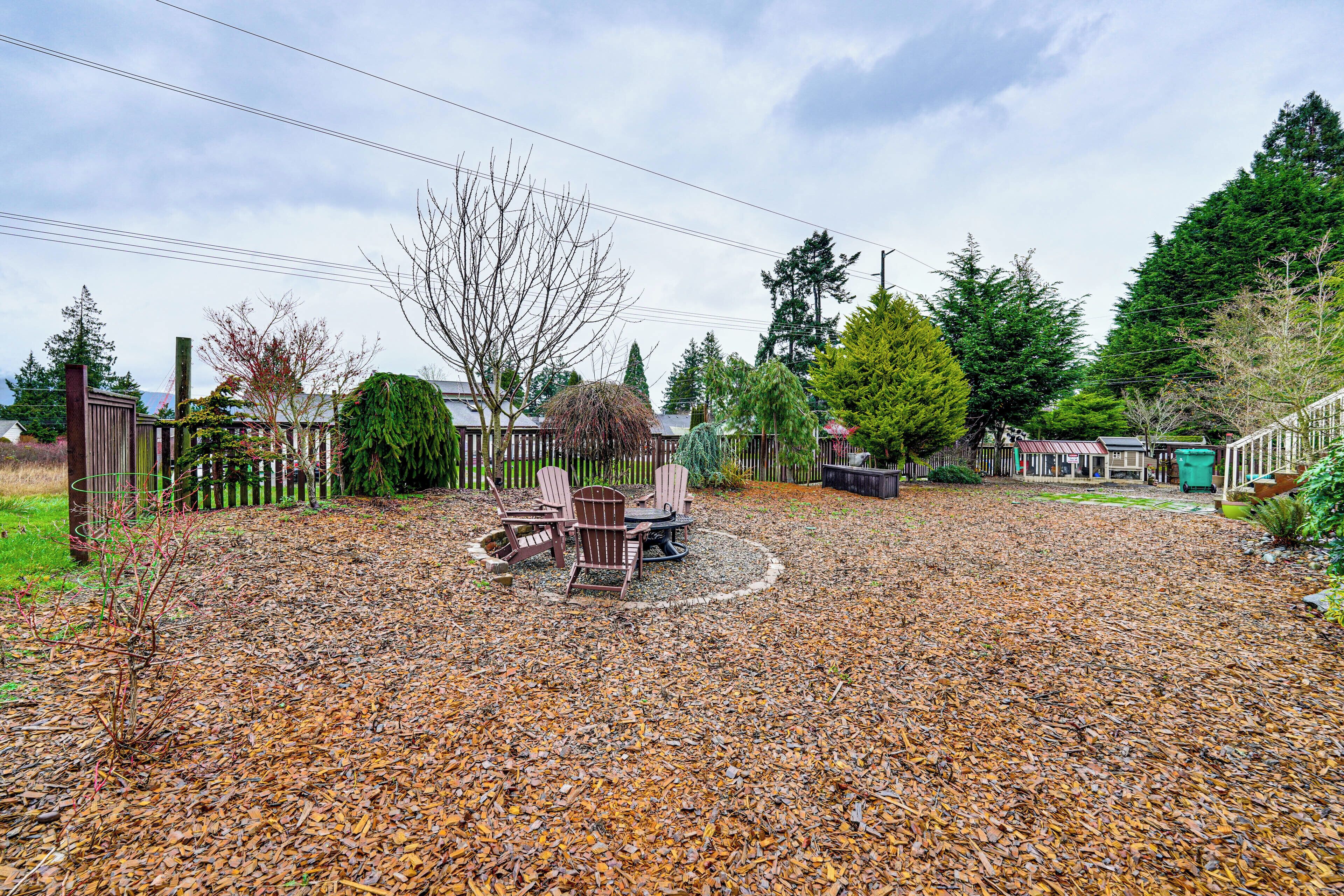 A patio area with a table and chairs, surrounded by a wooden fence and various trees.