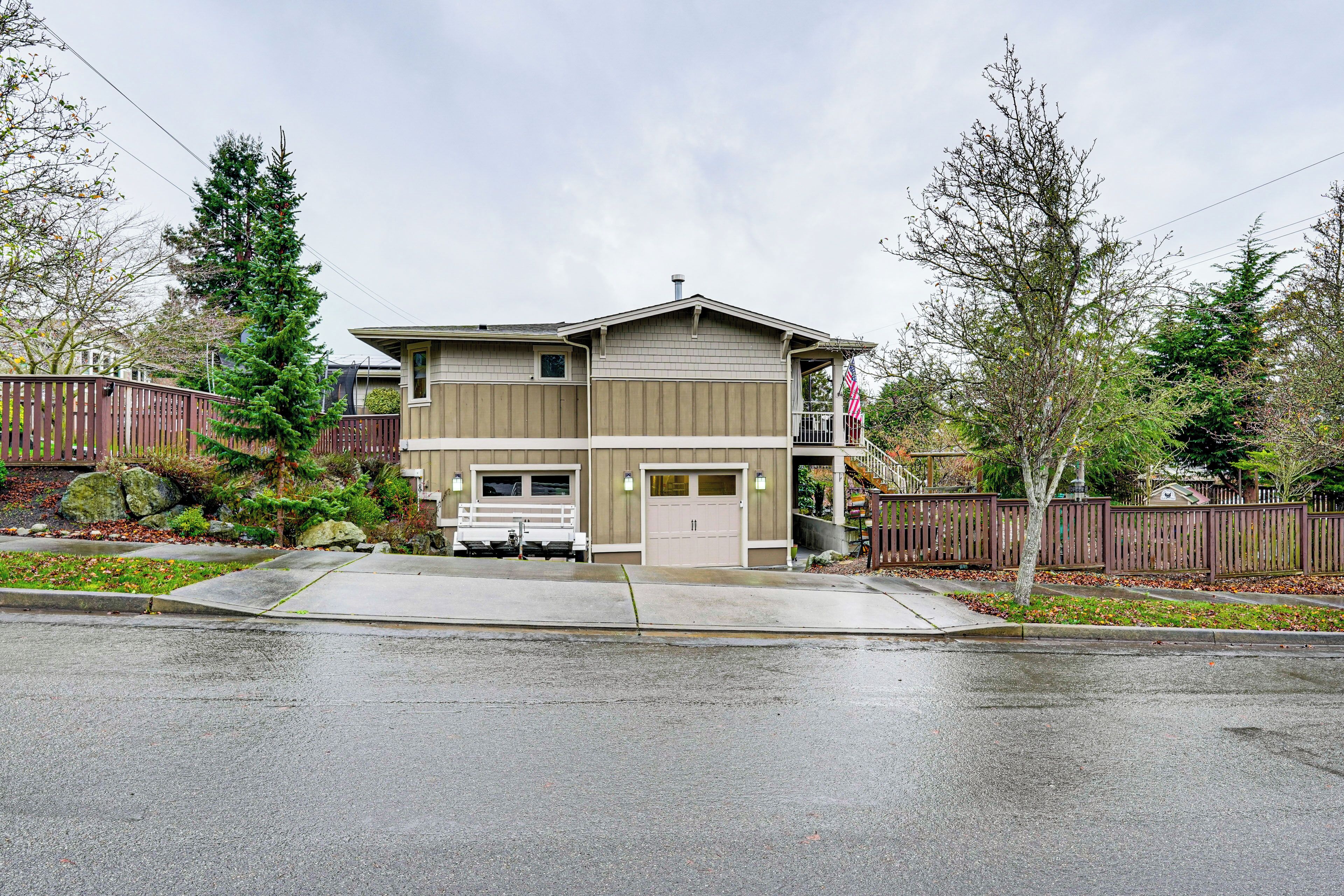 A two-story house with a garage, a driveway, and a front yard with trees and a fence.