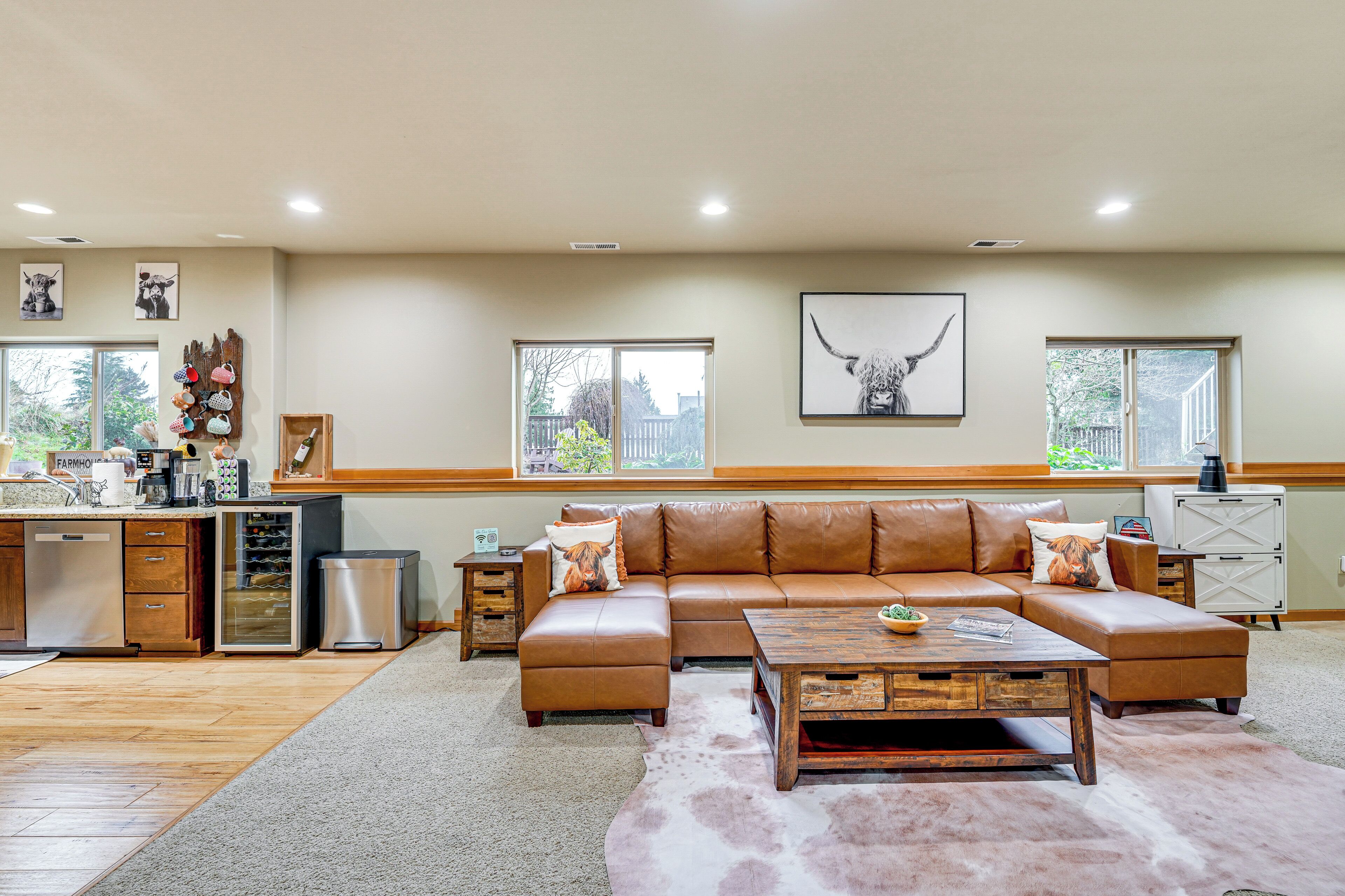 A spacious living room with a brown leather sectional sofa, a wooden coffee table, and a cowhide rug.