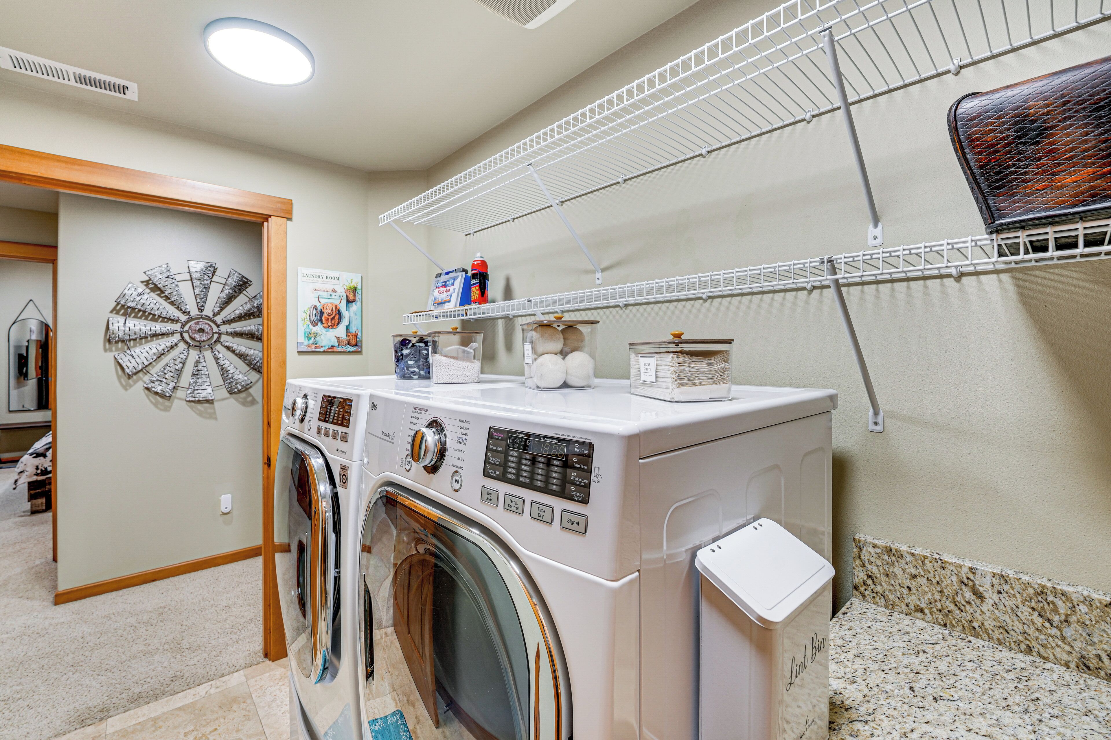 A laundry room with a front-loading washer and dryer, a drying rack, and a decorative wall piece.