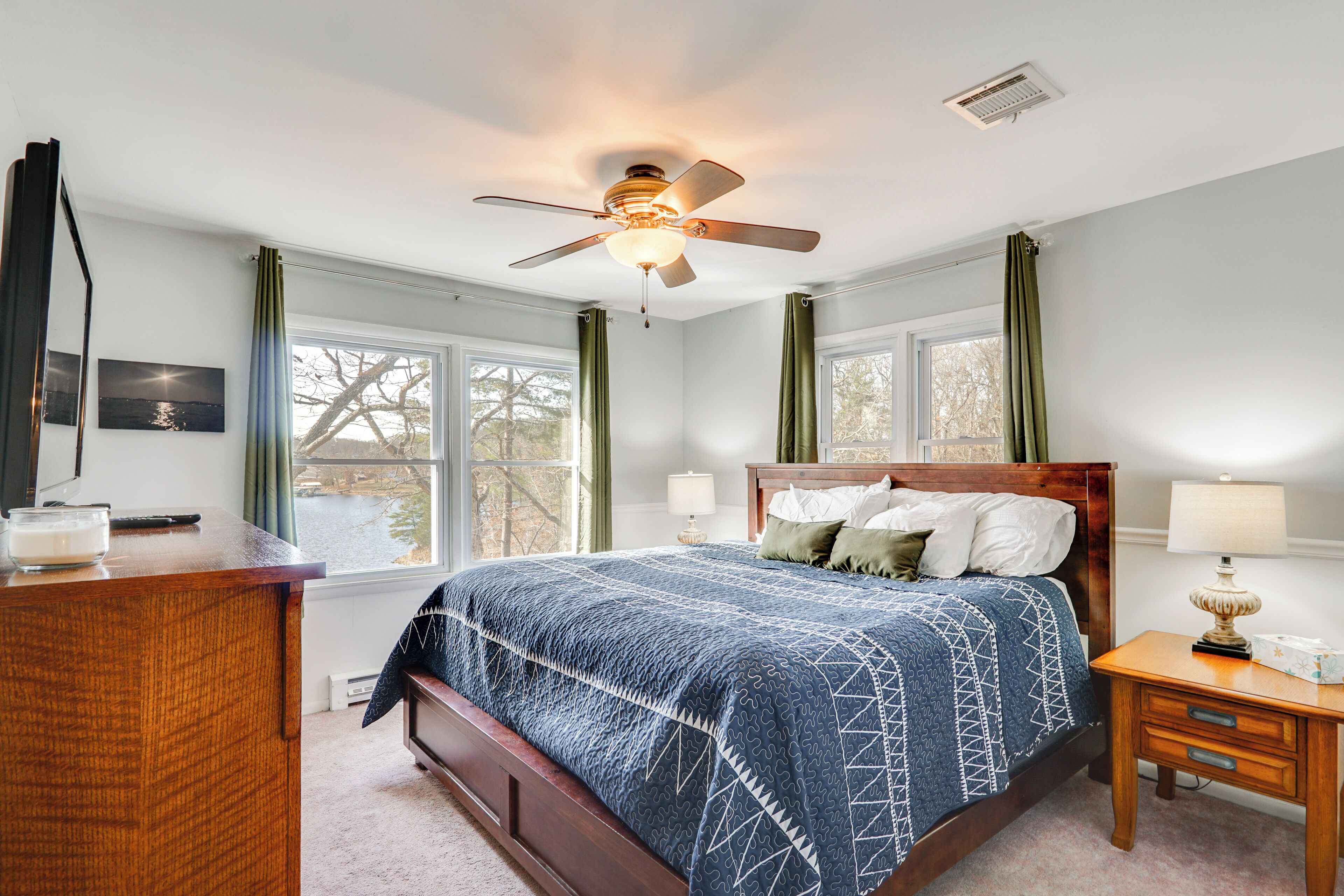 A bedroom with a bed, a desk, a chair, a ceiling fan, and a window with curtains.