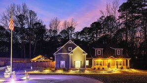 A two-story house with a porch and a well-lit driveway at dusk. - Gather, Play & Unwind! Modern Locust Grove Home (Locust Grove)