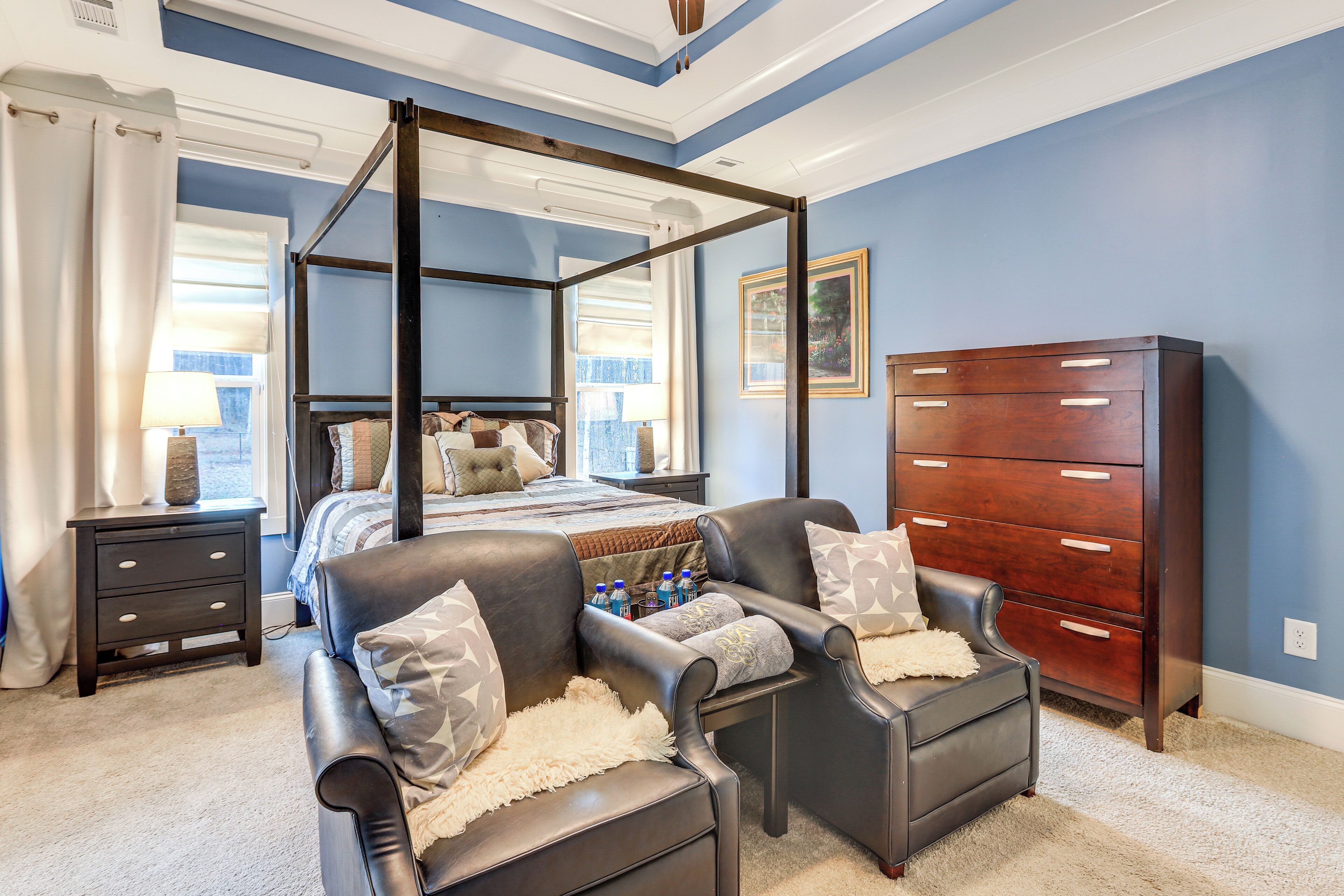 A bedroom with a four-poster bed, a dark wooden dresser, and a seating area with two chairs.