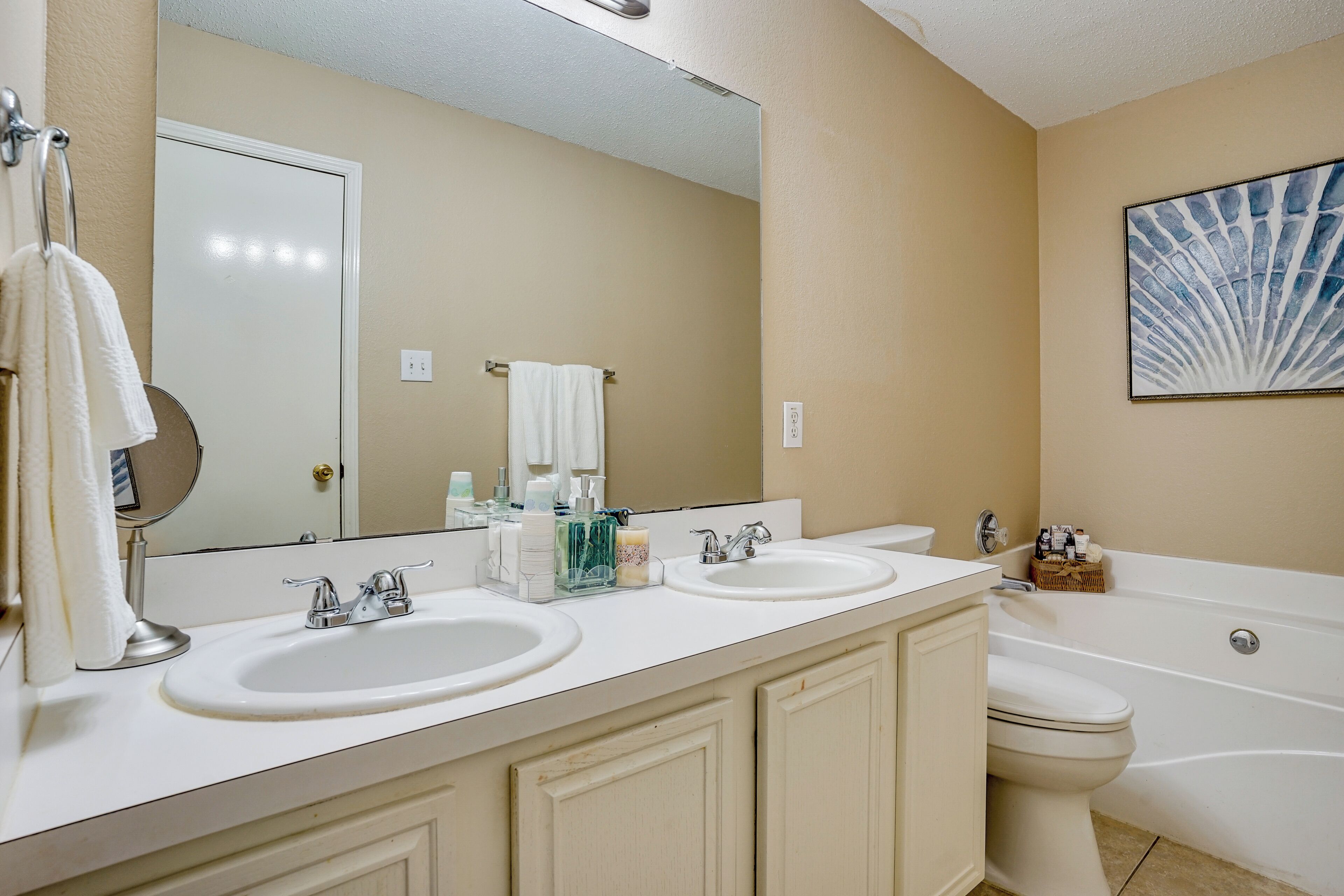 Une salle de bain avec deux lavabos, des toilettes et une baignoire. Un grand miroir est placé au-dessus des lavabos, et on peut voir un porte-serviettes sur la gauche.