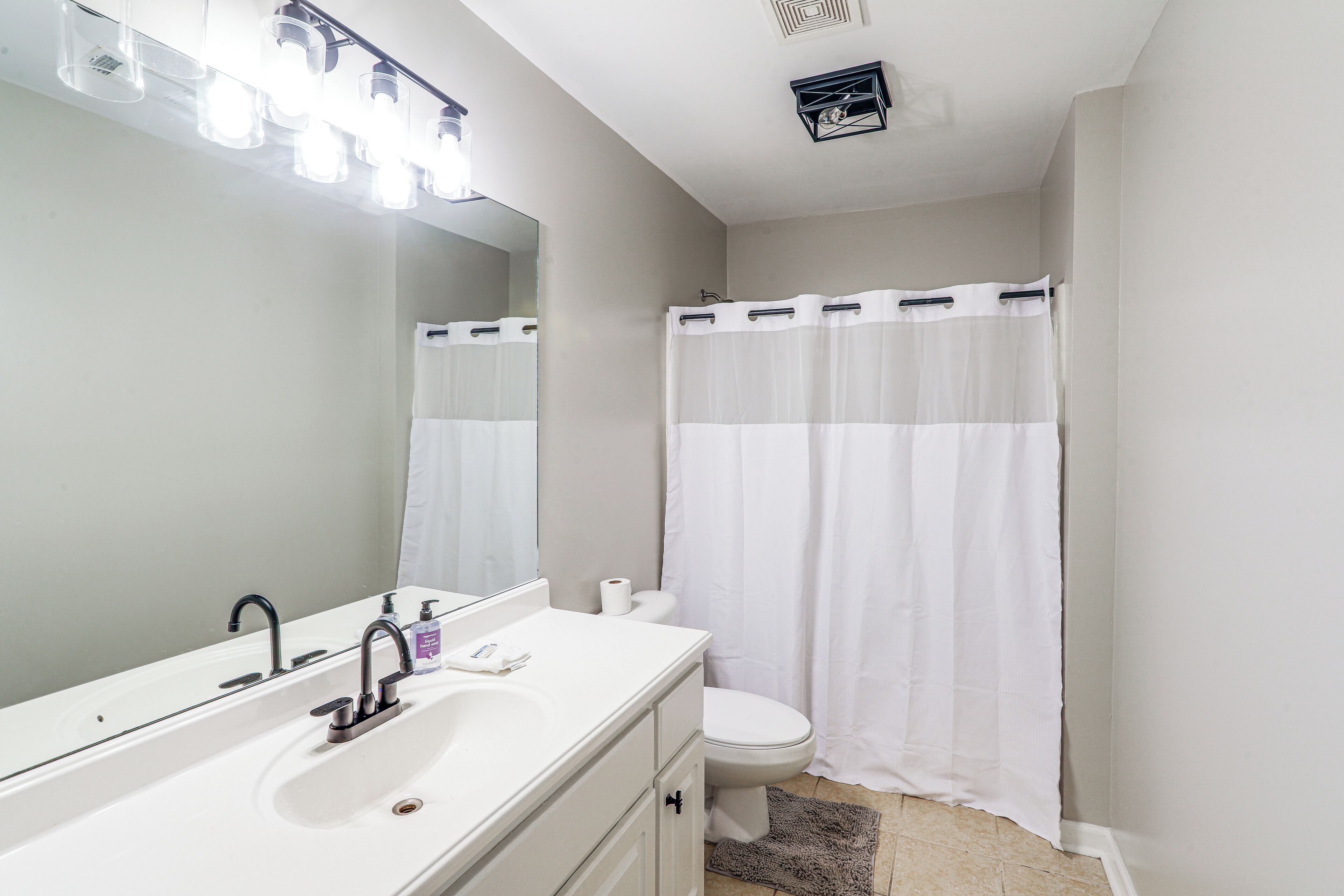 A bathroom with a white sink, two faucets, a mirror, and a shower curtain.