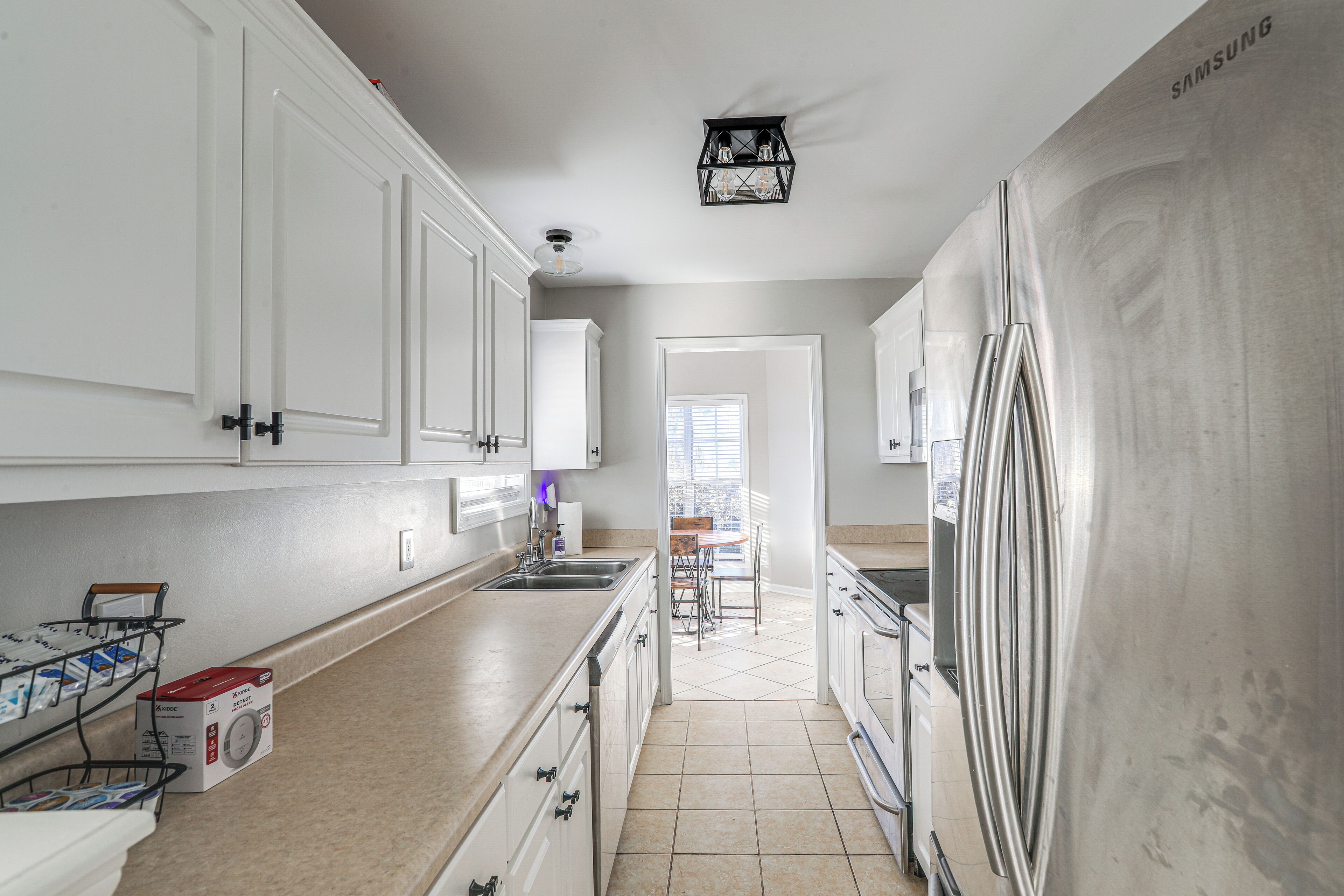 A modern kitchen with white cabinets, a stainless steel refrigerator, and a window providing natural light.