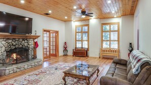 A spacious living room with a stone fireplace, wooden ceiling, and large windows. - Games Galore! Pine Mountain Club Retreat Near Town (Pine Mountain Club)