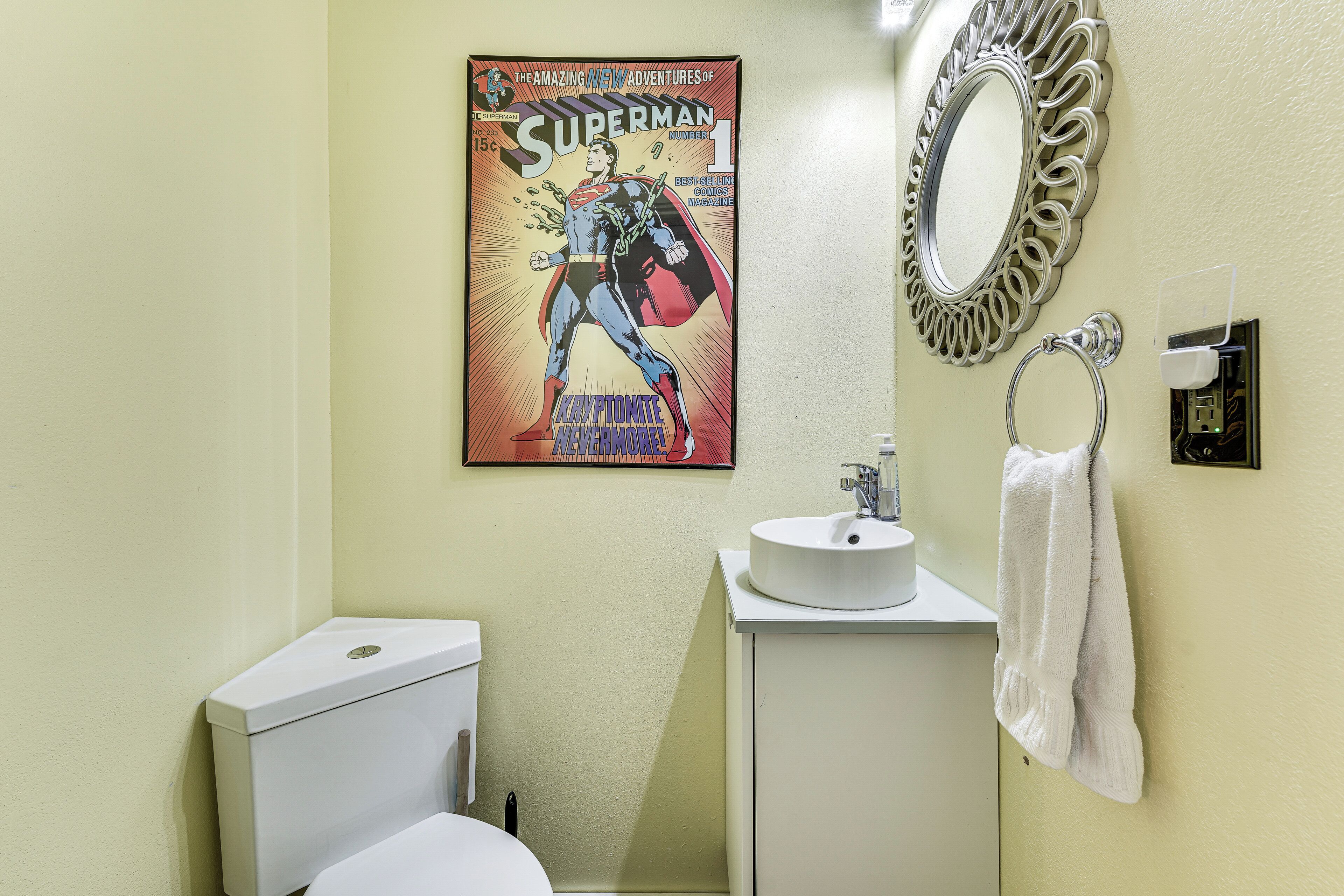 A bathroom with a toilet, sink, mirror, and a Superman comic book on the wall.