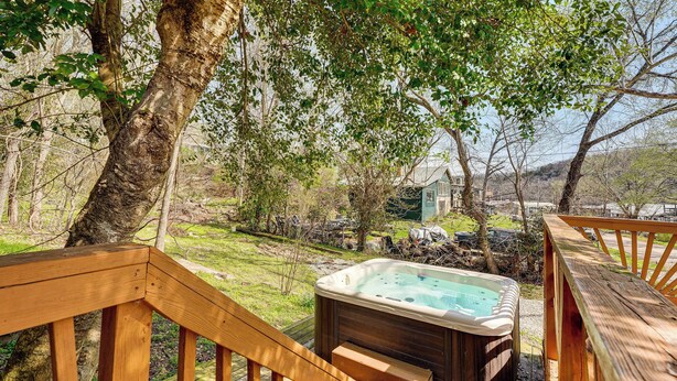 Une terrasse en bois avec un jacuzzi, entourée d’arbres et d’une pelouse.