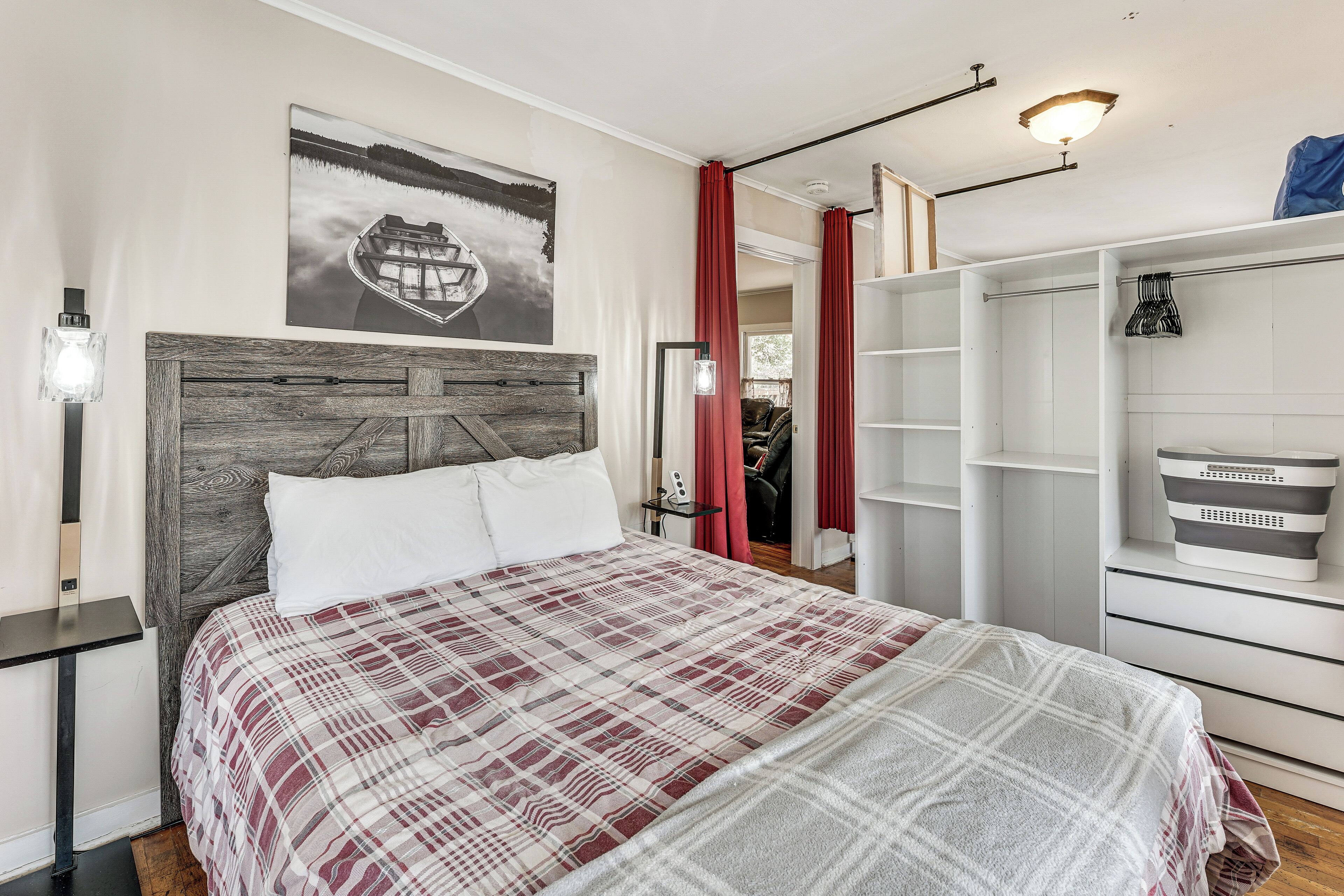 A bedroom with a bed, a headboard, a wardrobe, a nightstand, a lamp, and a painting on the wall.