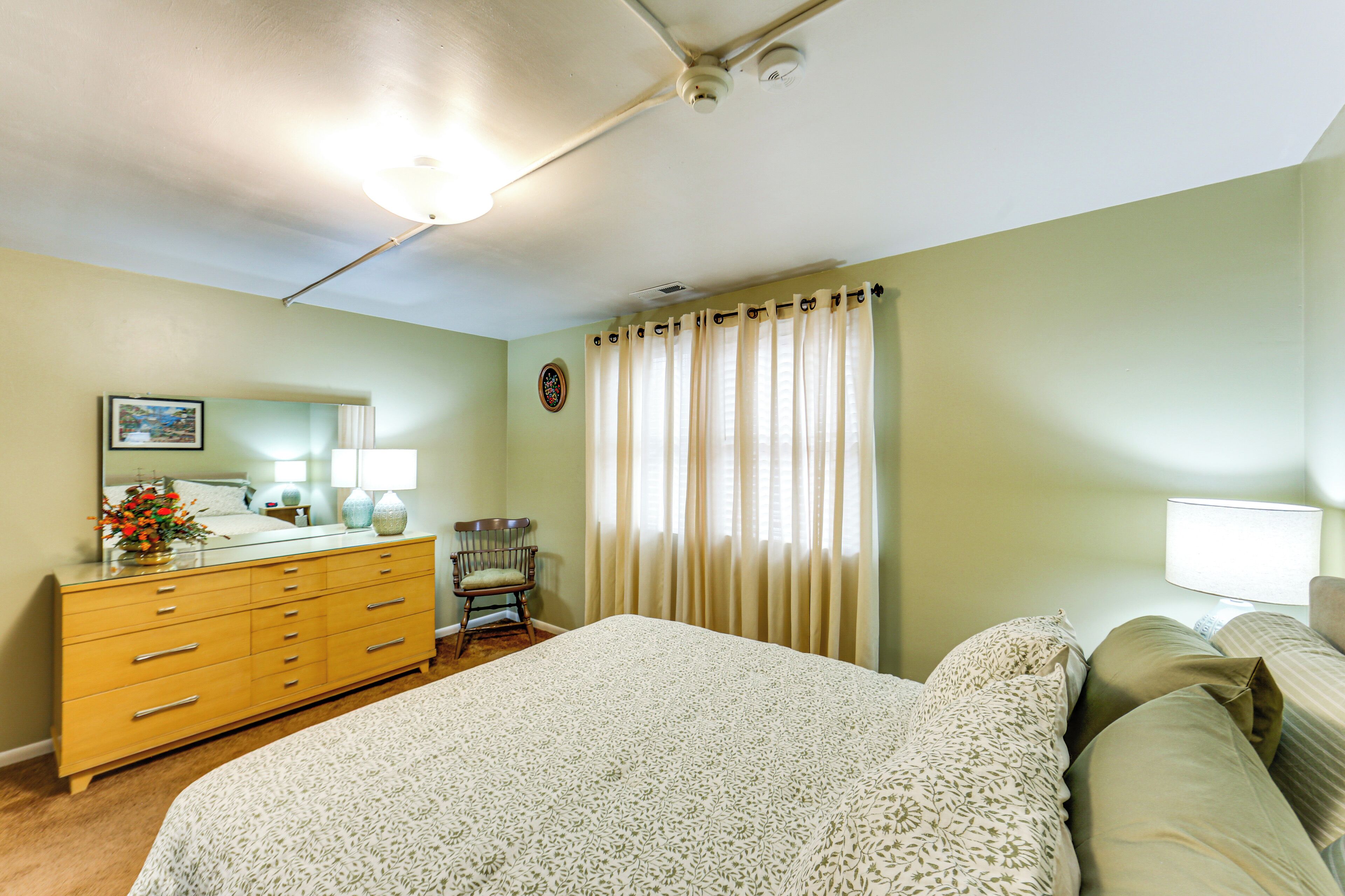 Une chambre à coucher avec un lit, une commode, une chaise et une fenêtre avec des rideaux.