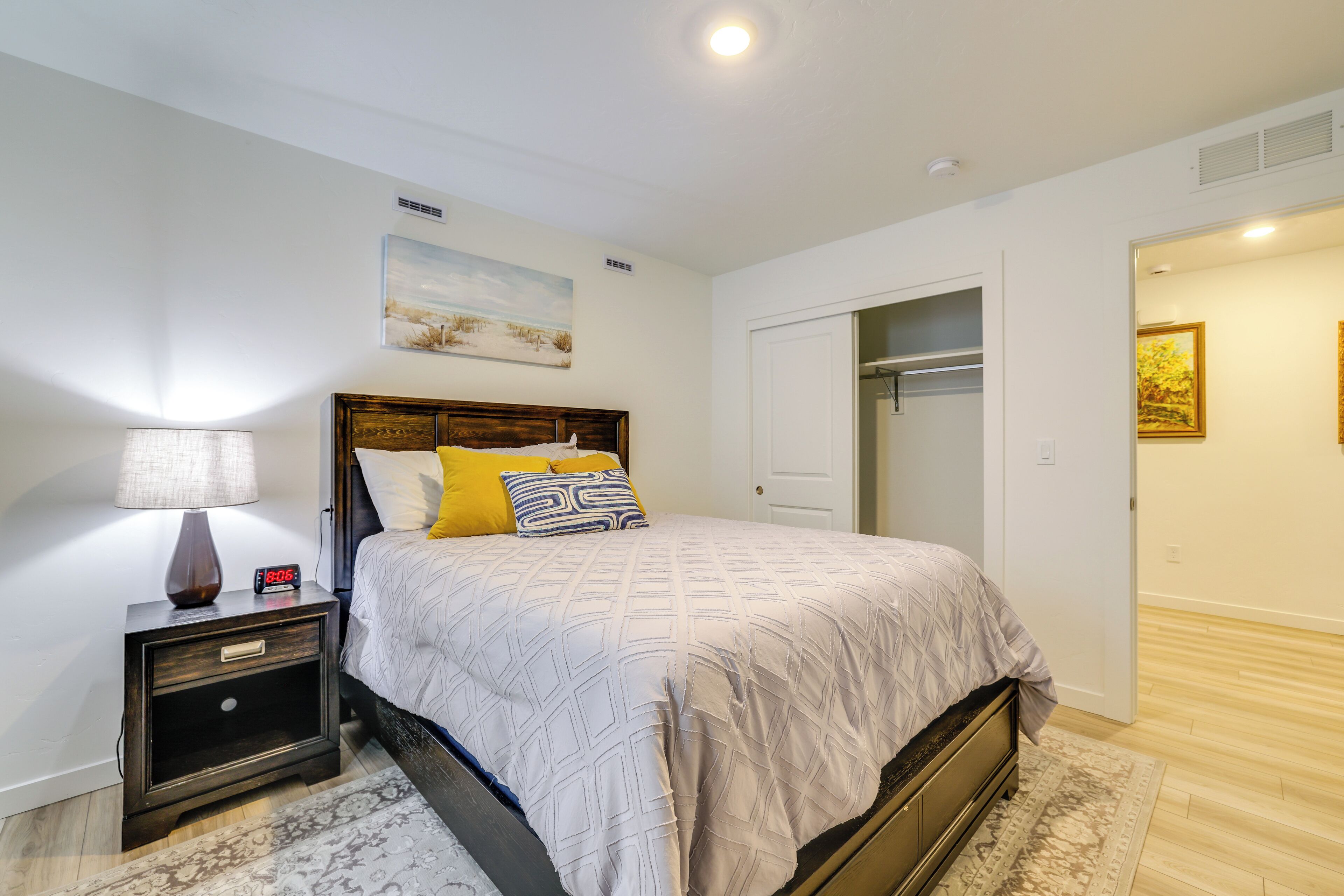 A bedroom with a bed, nightstand, lamp, and a painting on the wall.