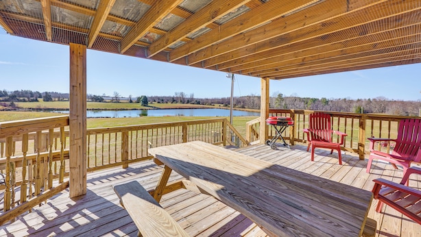 A wooden deck with a picnic table and red chairs, overlooking a lake. - 100-acre Family Getaway in Kenbridge: Pets Welcome (Kenbridge)