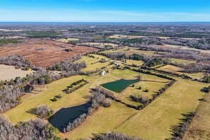 An aerial view of a rural landscape with fields, a pond, and scattered trees. - 100-acre Family Getaway in Kenbridge: Pets Welcome (Kenbridge)
