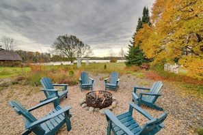 A circular seating arrangement around a fire pit with a lake and autumn foliage in the background. - Copper Moose Cottage Historic Home w/ Game Room (Michigamme)