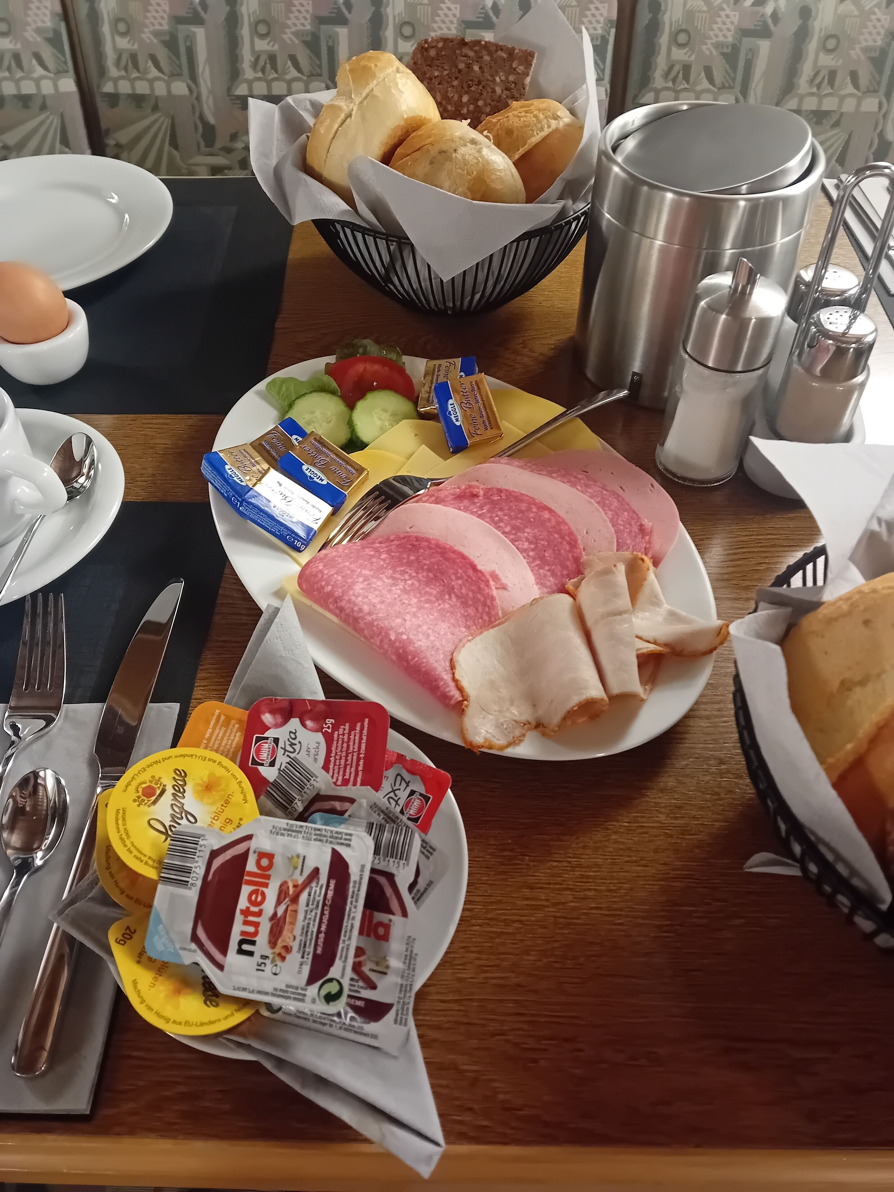 Une table de petit-déjeuner avec du pain, du jambon, du fromage et des condiments.