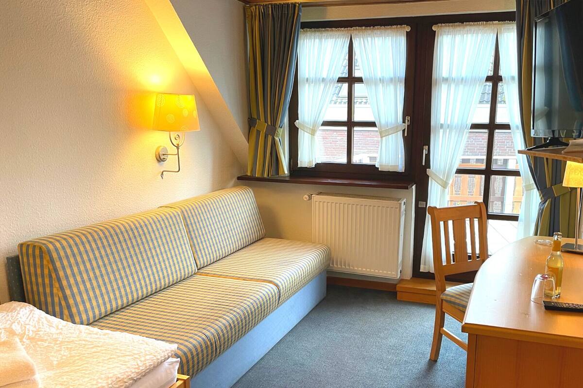 A cozy room with a striped sofa, a wooden chair, a small table with a bottle and glass, and a window with curtains.