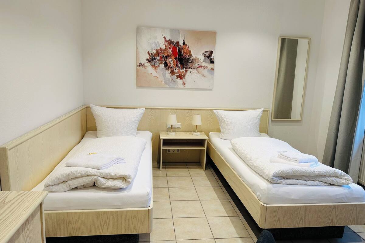 A hotel room with two single beds, a nightstand with lamps, a painting on the wall, and a mirror.