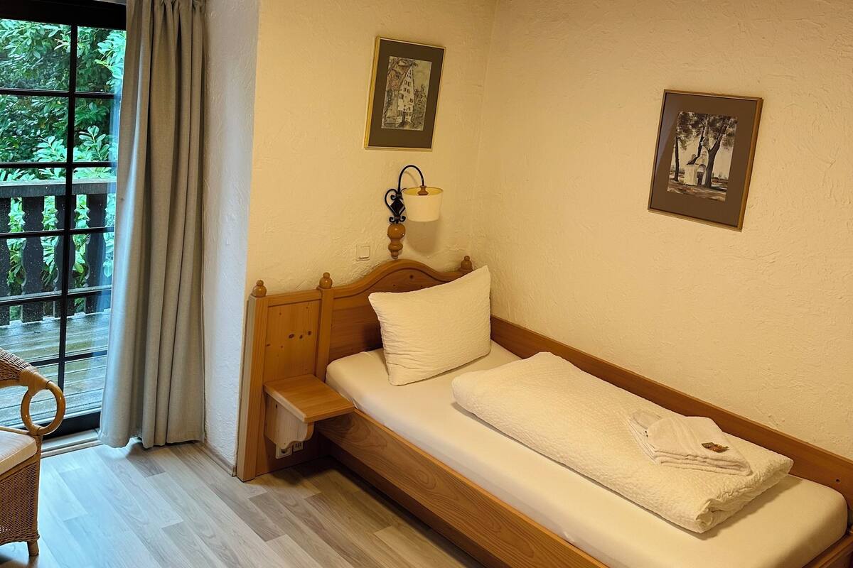 A single bed with a wooden headboard, a bedside table, a lamp, and two framed pictures on the wall.