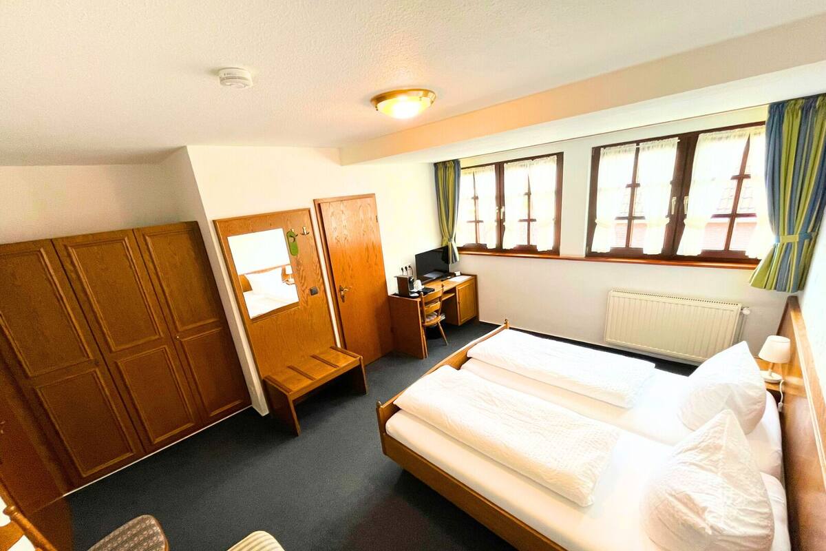 A hotel room with a bed, a desk, a chair, a wardrobe, and a window with curtains.