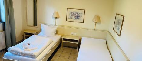 Une chambre d’hôtel avec un lit simple, un petit lit, deux tables de chevet, une commode, une lampe, un miroir et deux tableaux encadrés accrochés au mur.