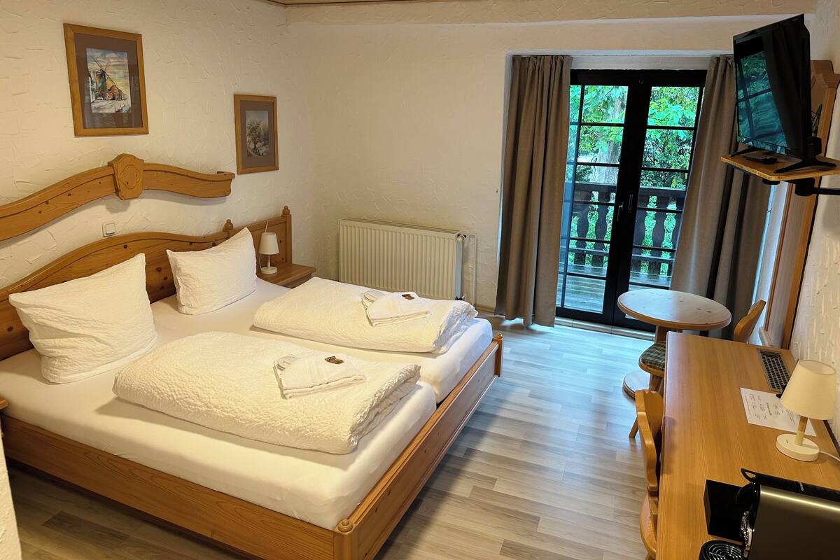A hotel room with a wooden bed, a desk, a chair, a TV, and a window with curtains.