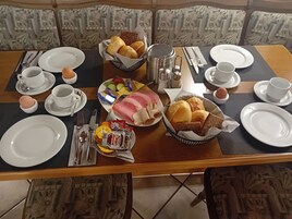 Uma mesa de jantar posta com pratos, talheres, pão, ovos e acompanhamentos.