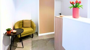 A modern room with a green sofa, a small round table with a plant, and a pink vase with flowers on a white counter.