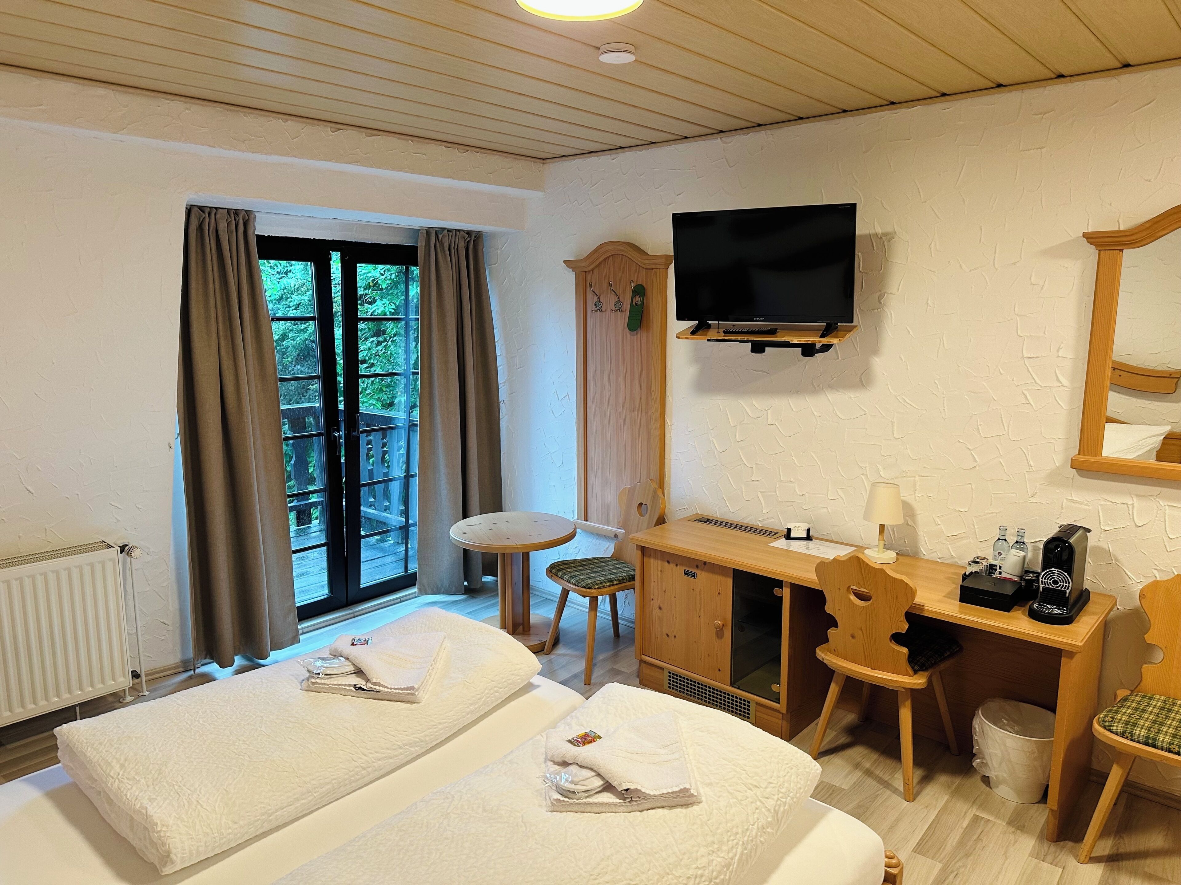 A hotel room with two beds, a desk with a chair, a television, and a window with curtains.