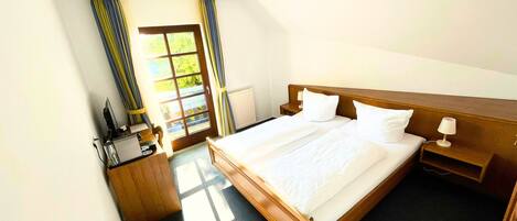 Ein Hotelzimmer mit einem großen Bett, einem Holz-Kopfteil, einem Nachttisch mit Lampe und einem Fenster mit Vorhängen.