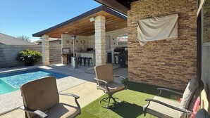 A covered outdoor area with a pool, two lounge chairs, and a ceiling fan.