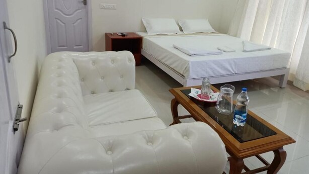 A hotel room with a white sofa, a bed with white bedding, a wooden coffee table with a glass, a bottle, and a small tray.