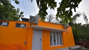 A small, single-story building with a bright orange exterior, a white door, and a small window.