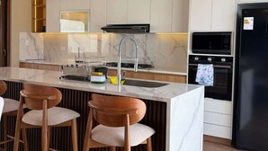 Una cocina moderna con encimera de mármol, electrodomésticos de acero inoxidable y taburetes de bar de madera.