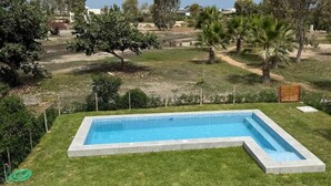 Una piscina rectangular con borde de hormigón, rodeada por un césped cuidado y diferentes árboles.