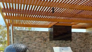Una cocina exterior con una parrilla integrada, un lavamanos grande y un salpicadero con mosaicos.