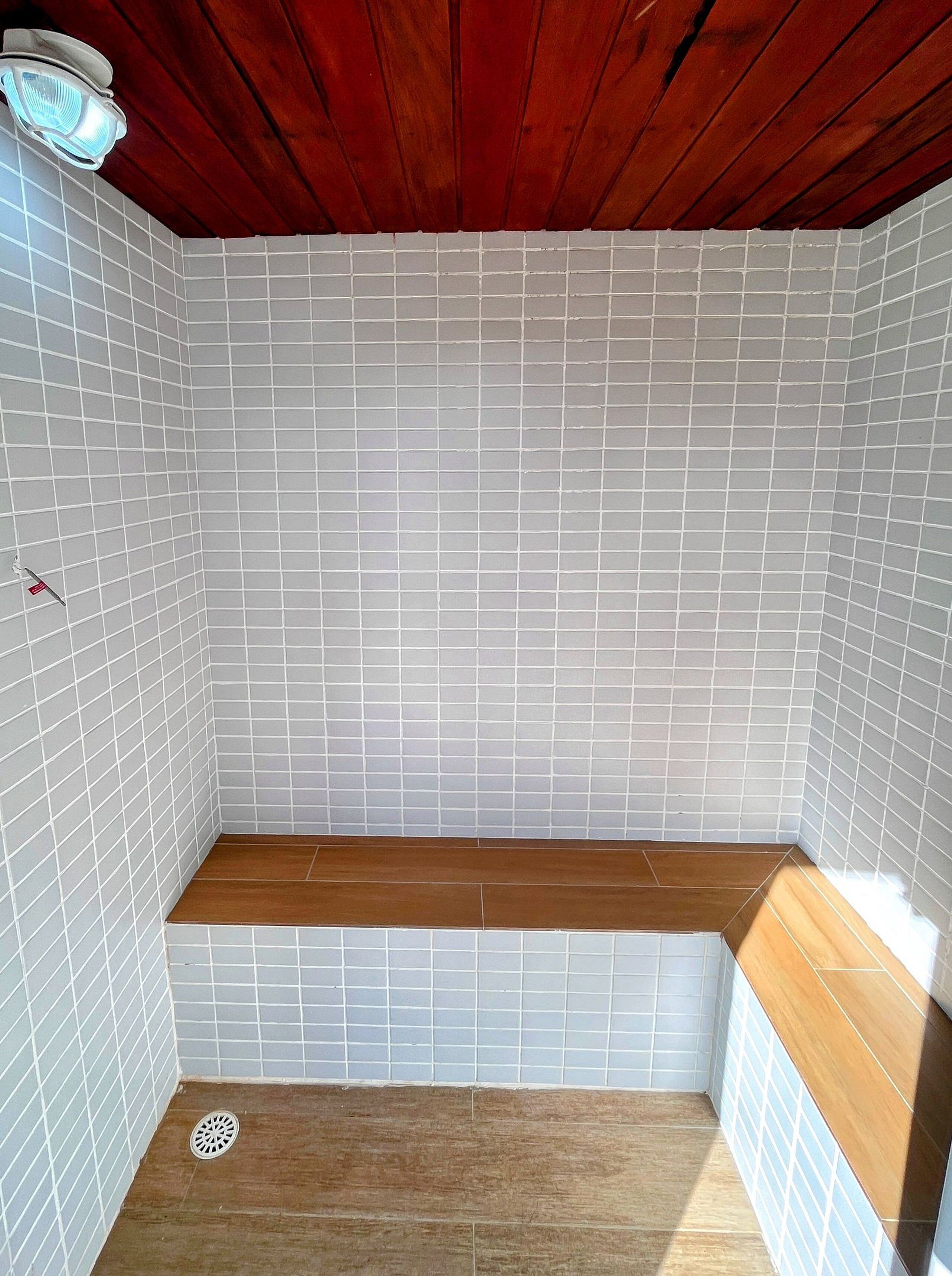 Un petit espace douche fermé, avec des murs carrelés et un banc en bois.
