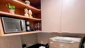 A compact kitchen with a microwave, coffee maker, and wine glasses on shelves. - Cupe Living - VSH (Ipojuca)