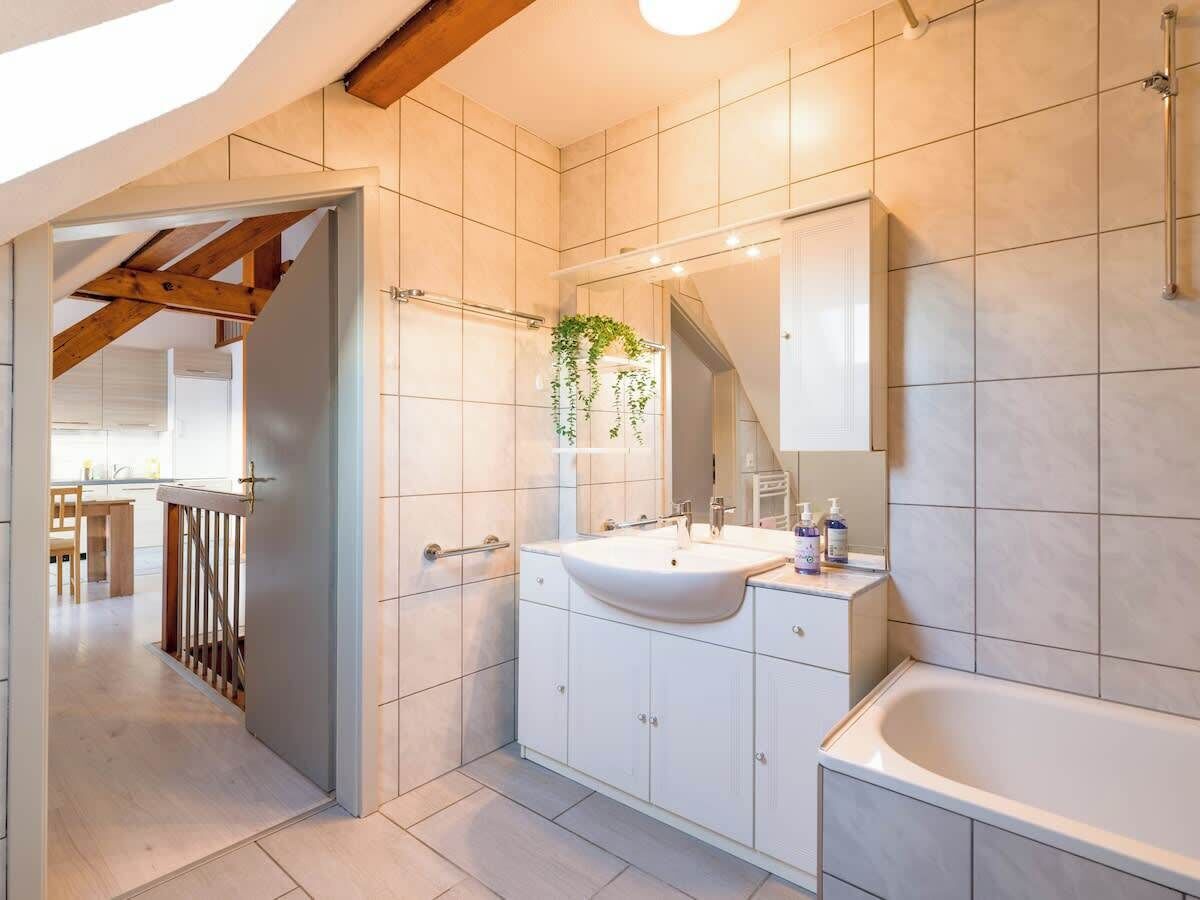 Een moderne badkamer met een groot wastafel, een badkuip en een spiegel. Een houten trap leidt naar een andere kamer.